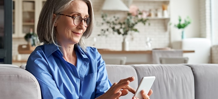 A woman sitting on her couch using the CenterWell Pharmacy mobile app to create med reminders